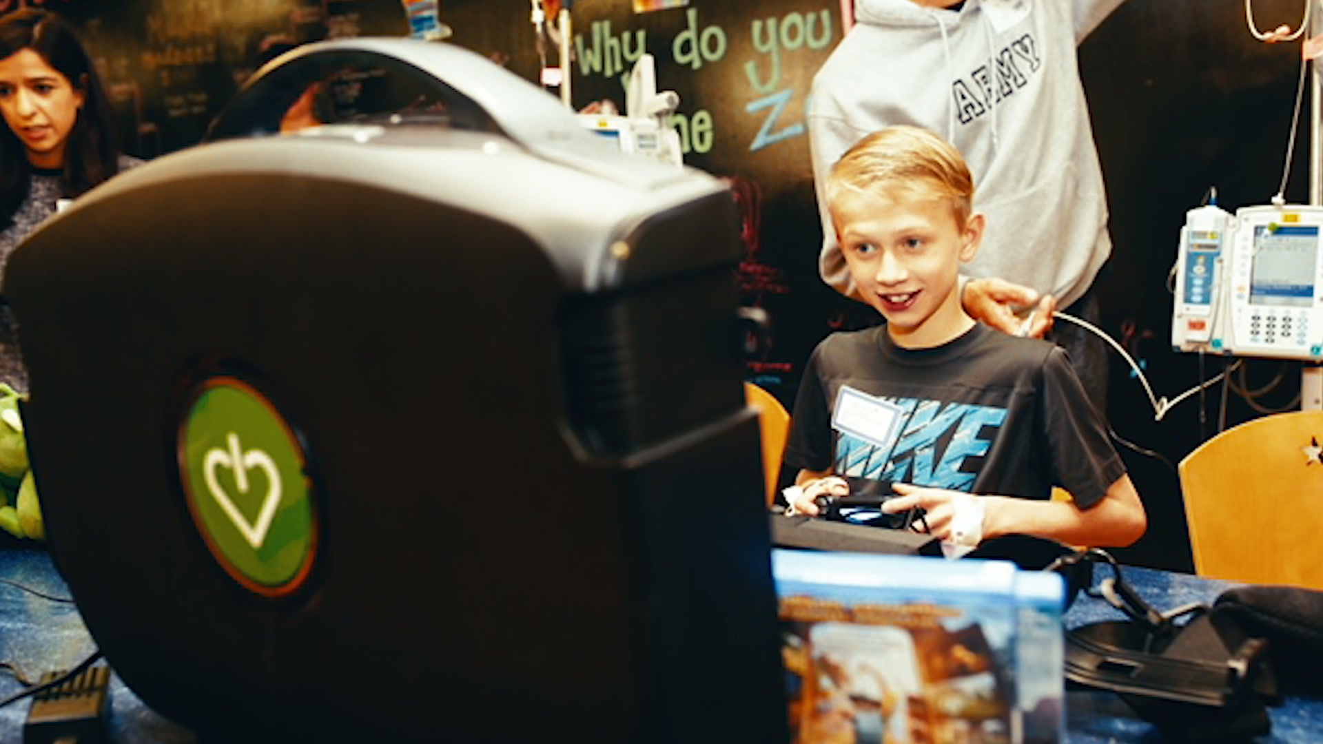 A boy smiling with a game controller at a GameChanger station in a hospital playroom.