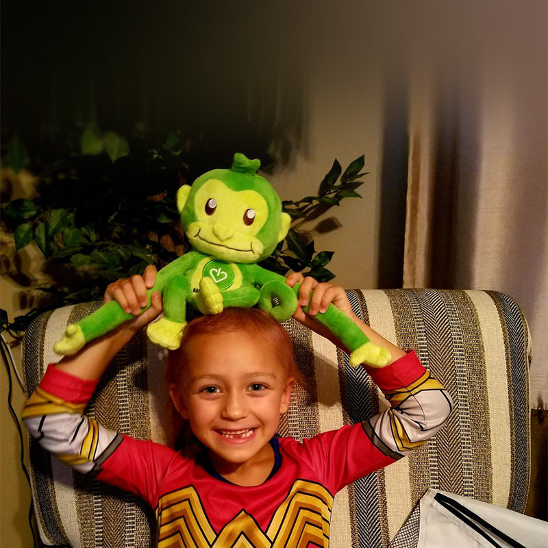 A beaming young patient holding Hope, GameChanger's green monkey, above their head.