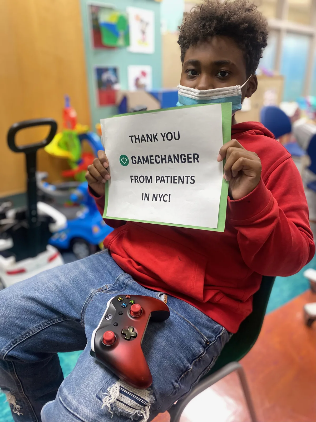 A young patient in a hospital playroom holding a hand-made ‘Thank you, GameChanger’ sign.