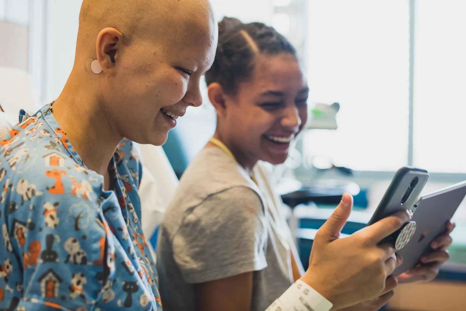 Two young patients laughing together over a tablet in the hospital.